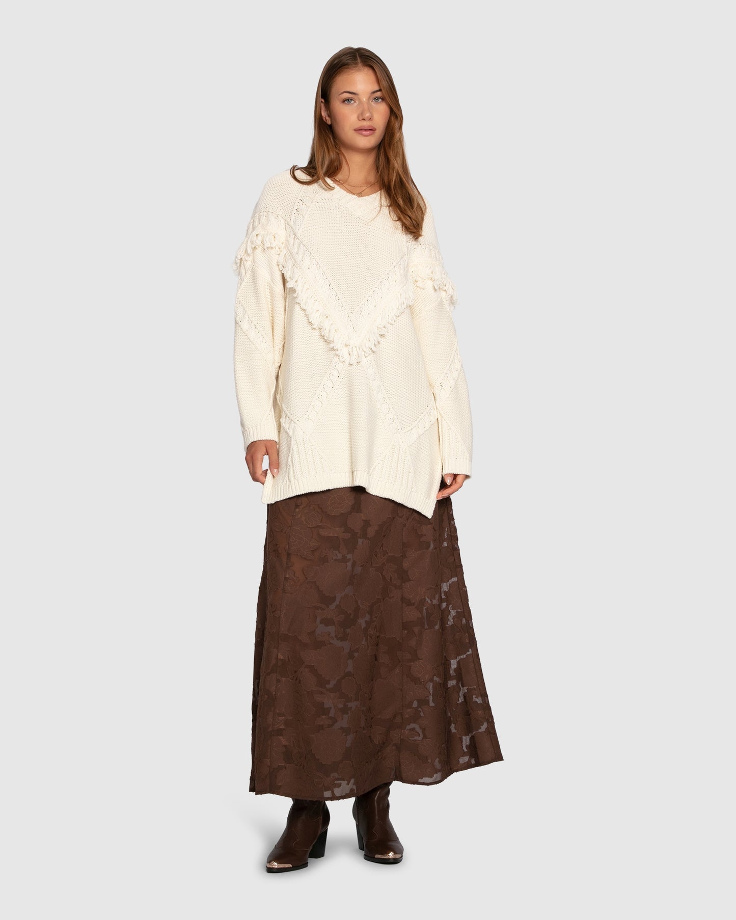Woman wearing a cream sweater and brown lace skirt on a white background