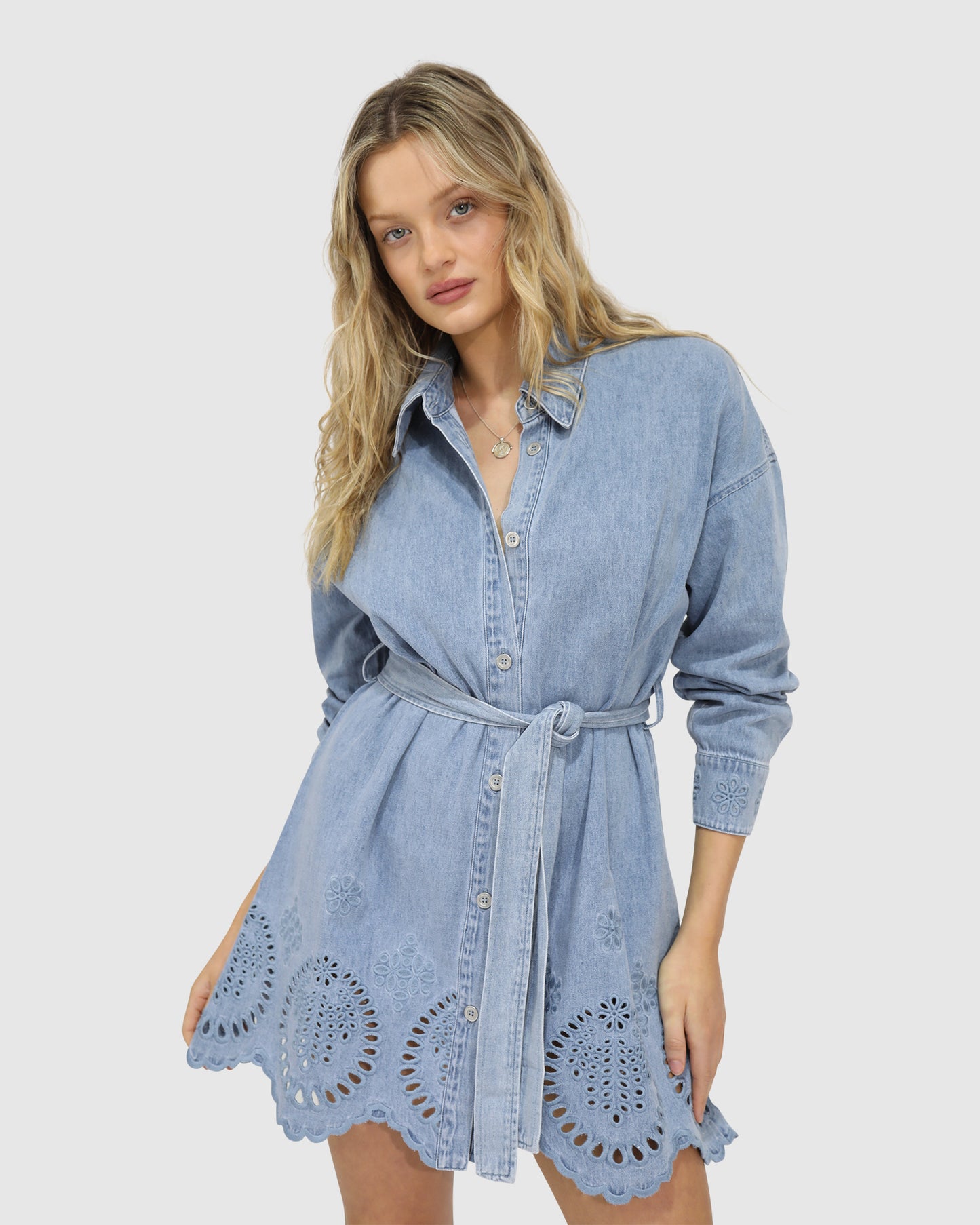 Model wearing the Sunday Somewhere Denim Broderie Shirt Mini Dress by Belle & Bloom – mini length, puff sleeves, button-down front, broderie anglaise details