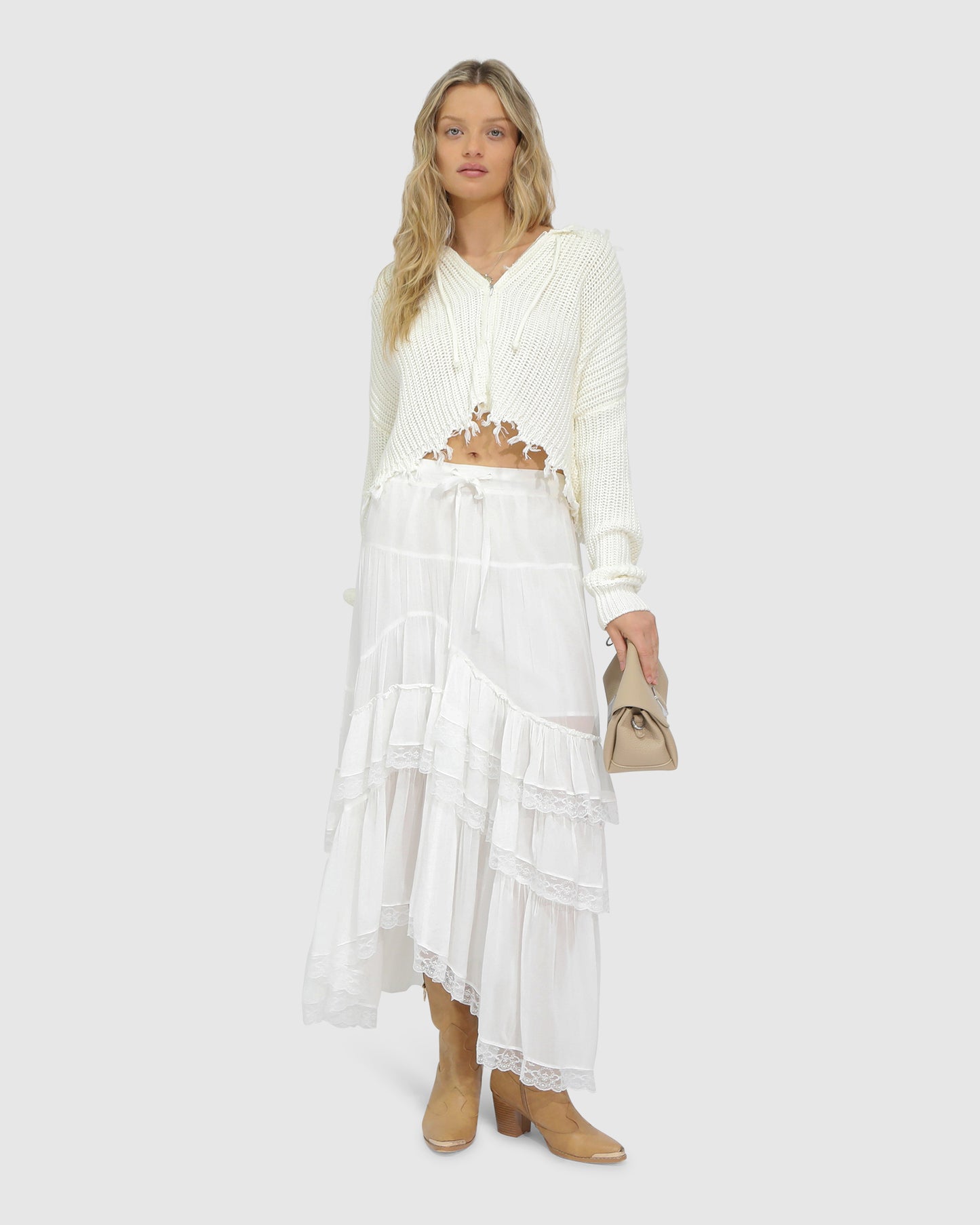 Woman wearing the Another Love Fringe Knit Zip Cardigan in cream, featuring chunky knit texture, zip front, drawstring hood, and fringed cropped hem – Belle and Bloom knitwear.
