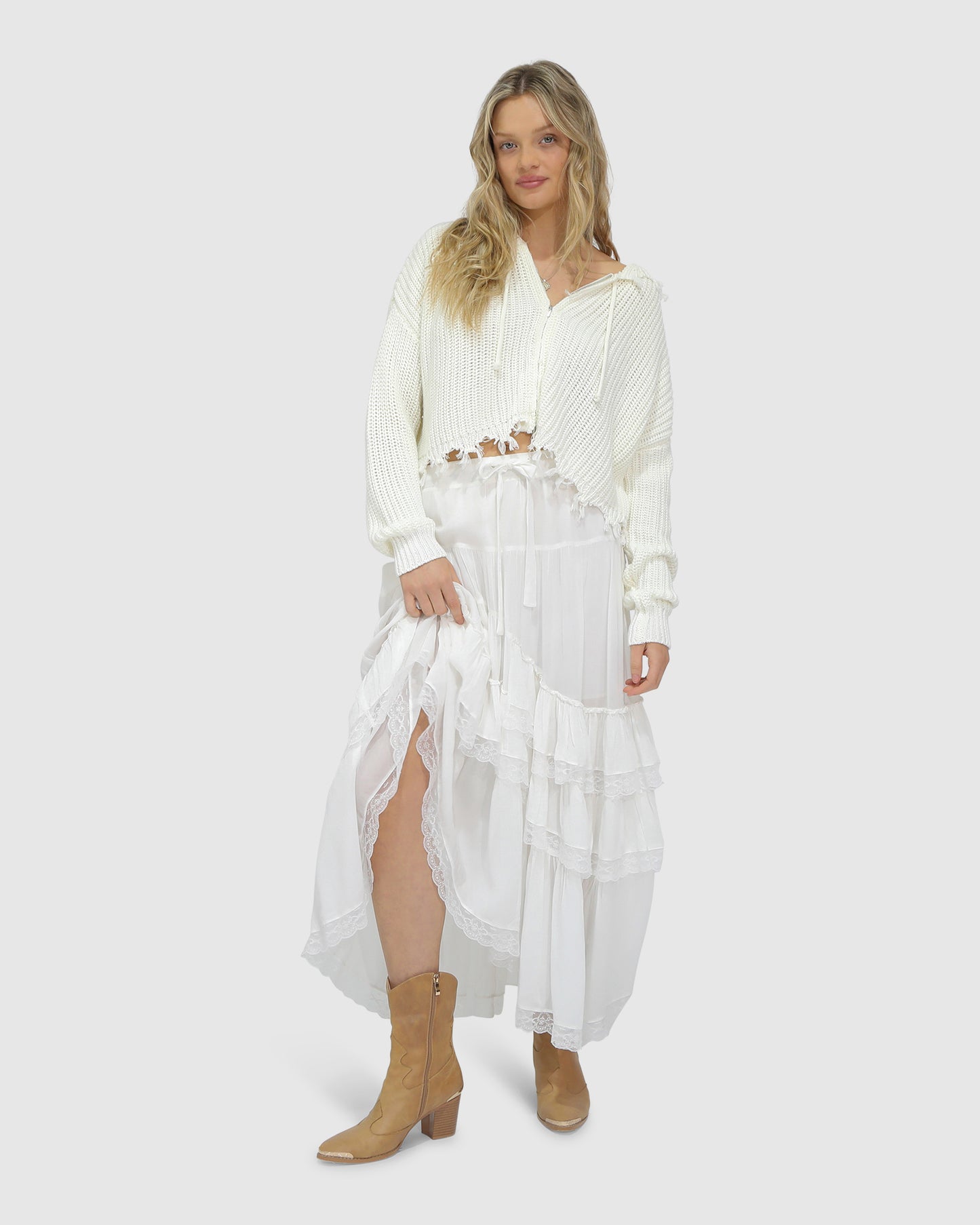 Woman wearing the Another Love Fringe Knit Zip Cardigan in cream, featuring chunky knit texture, zip front, drawstring hood, and fringed cropped hem – Belle and Bloom knitwear.