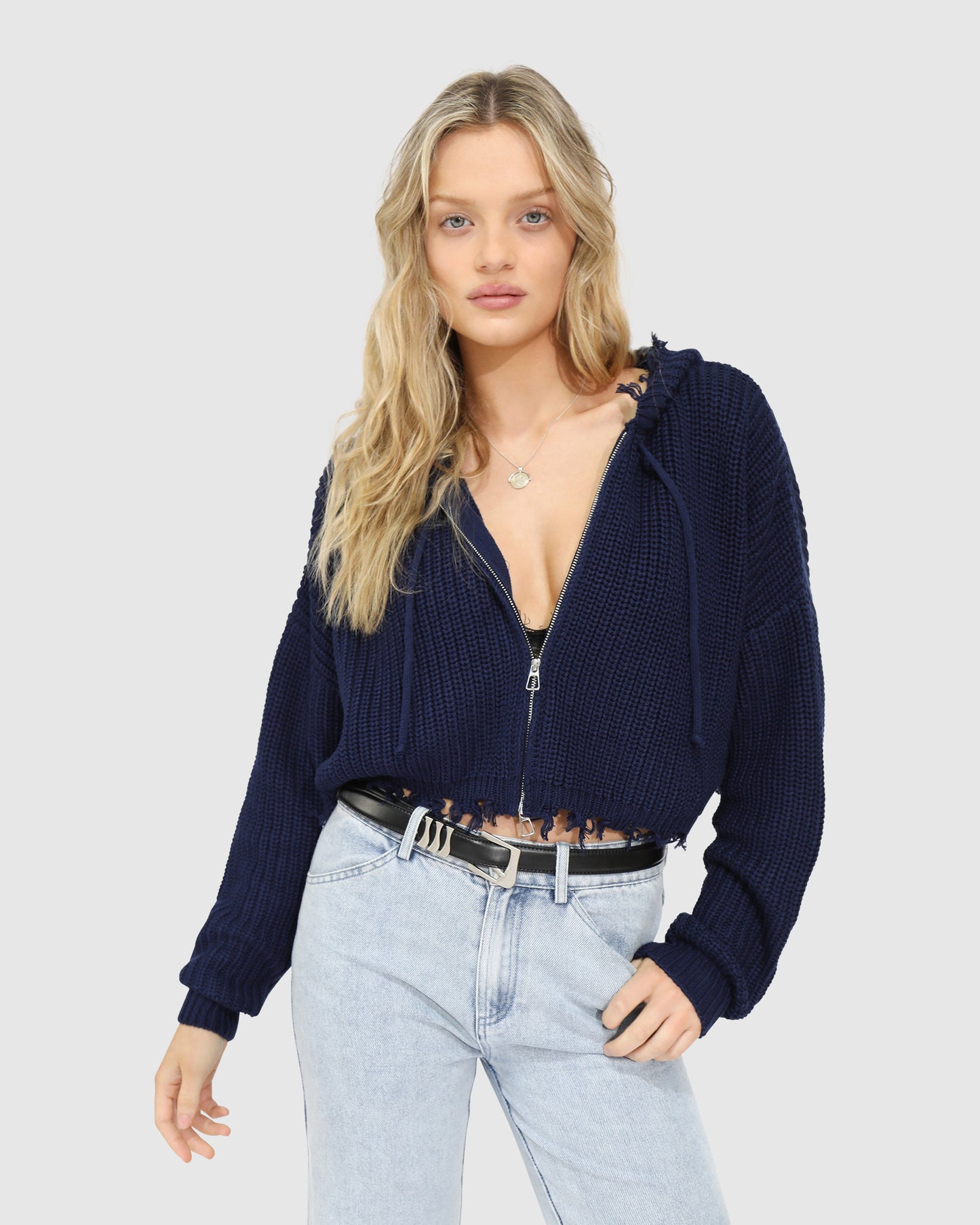 Woman wearing the Another Love Fringe Knit Zip Cardigan in navy, featuring chunky knit texture, zip front, drawstring hood, and fringed cropped hem – Belle and Bloom knitwear.