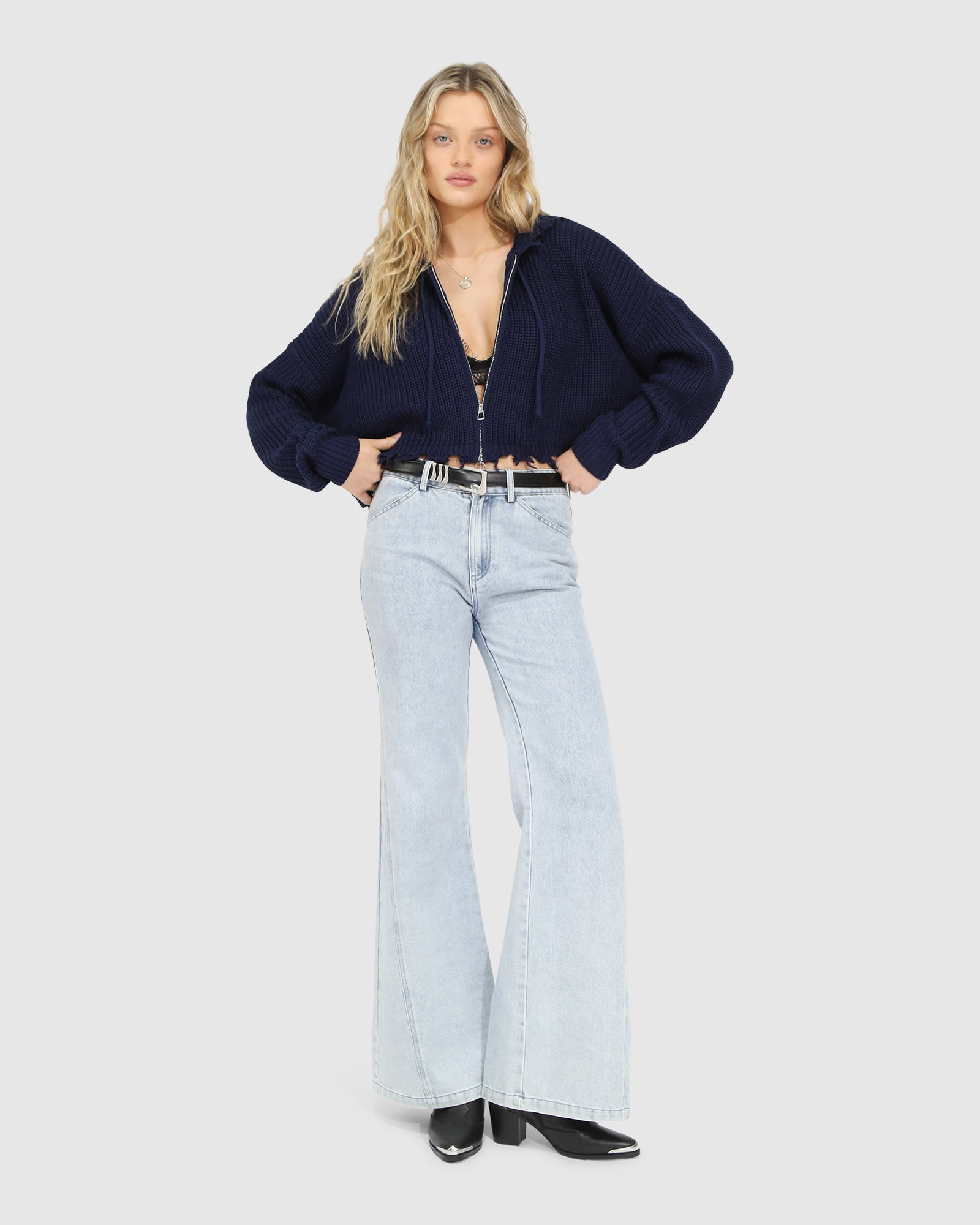 Woman wearing the Another Love Fringe Knit Zip Cardigan in navy, featuring chunky knit texture, zip front, drawstring hood, and fringed cropped hem – Belle and Bloom knitwear.