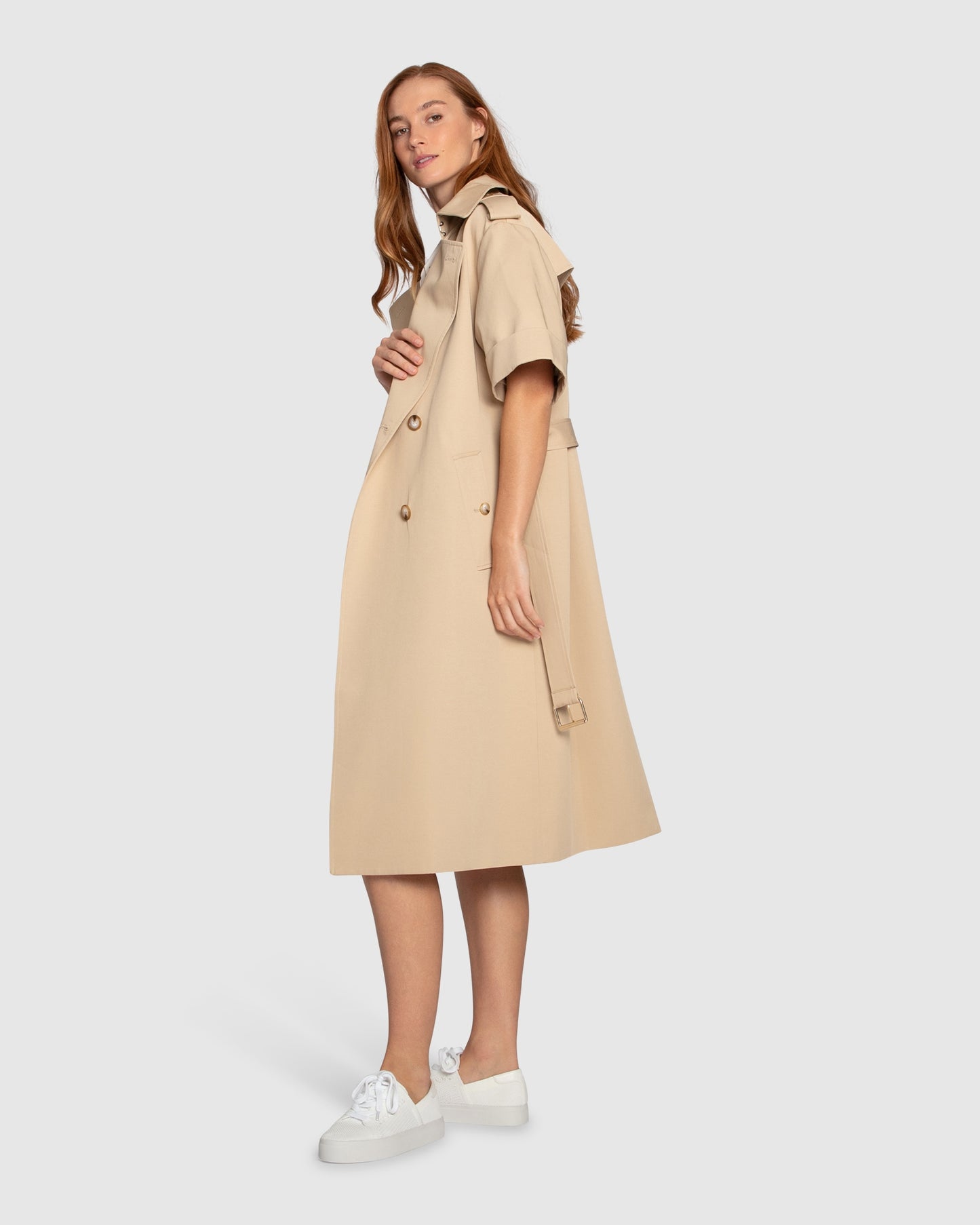 Side angle of Belle & Bloom Dust & Daring Short Sleeve Trench Style Dress in beige, showing short sleeves, belted waist and structured trench silhouette.