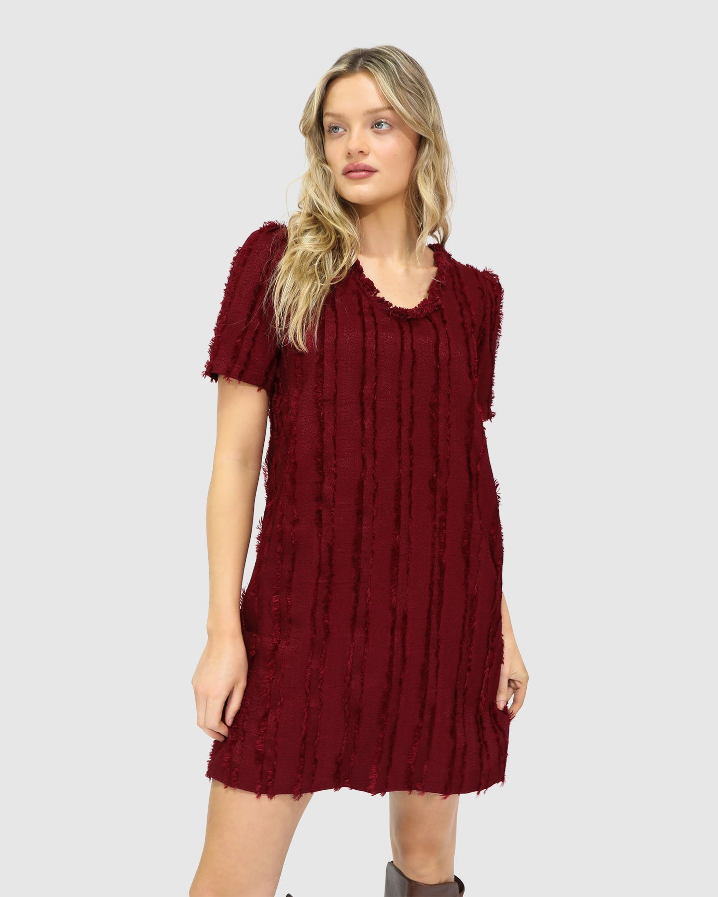 Woman wearing Belle & Bloom's burgundy-coloured Solana Boho Fringe Mini Shift Dress with a frayed V-neckline, textured sleeveless shift silhouette, side-seam pockets, and subtle fringe detail at the hem.