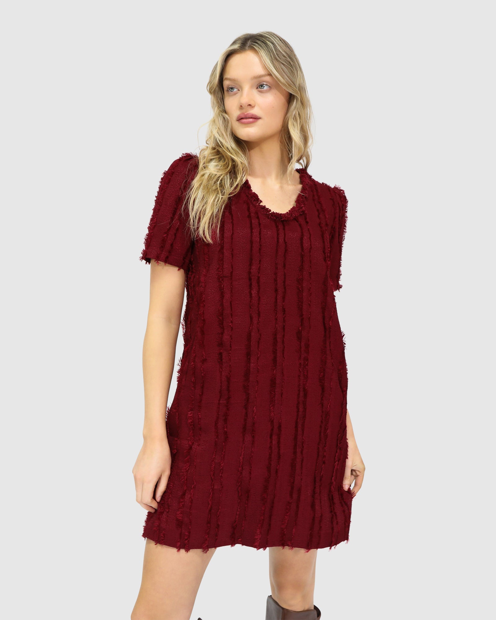 Woman wearing Belle & Bloom's burgundy-coloured Solana Boho Fringe Mini Shift Dress with a frayed V-neckline, textured sleeveless shift silhouette, side-seam pockets, and subtle fringe detail at the hem.