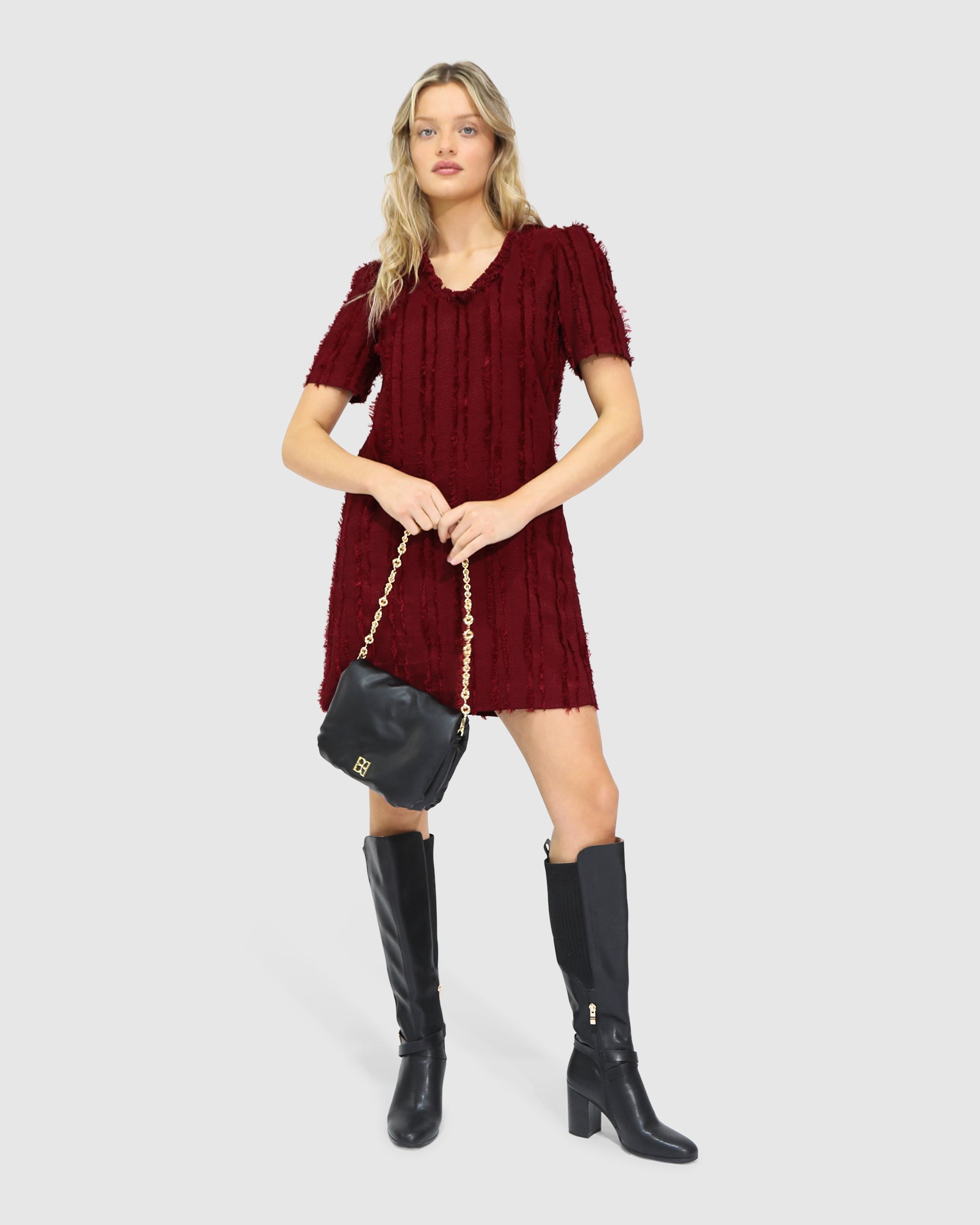 Woman wearing Belle & Bloom's burgundy-coloured Solana Boho Fringe Mini Shift Dress with a frayed V-neckline, textured sleeveless shift silhouette, side-seam pockets, and subtle fringe detail at the hem.