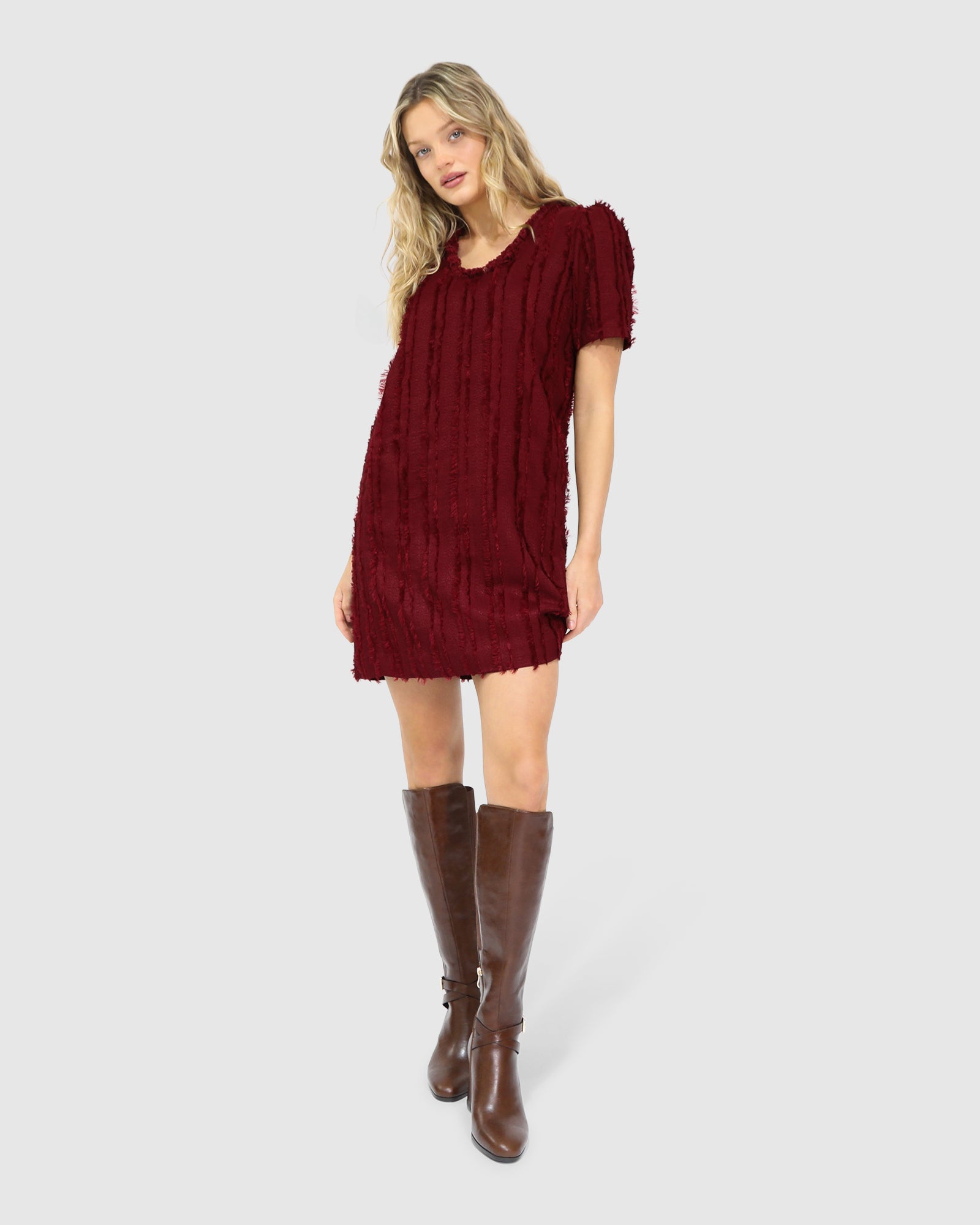 Woman wearing Belle & Bloom's burgundy-coloured Solana Boho Fringe Mini Shift Dress with a frayed V-neckline, textured sleeveless shift silhouette, side-seam pockets, and subtle fringe detail at the hem.