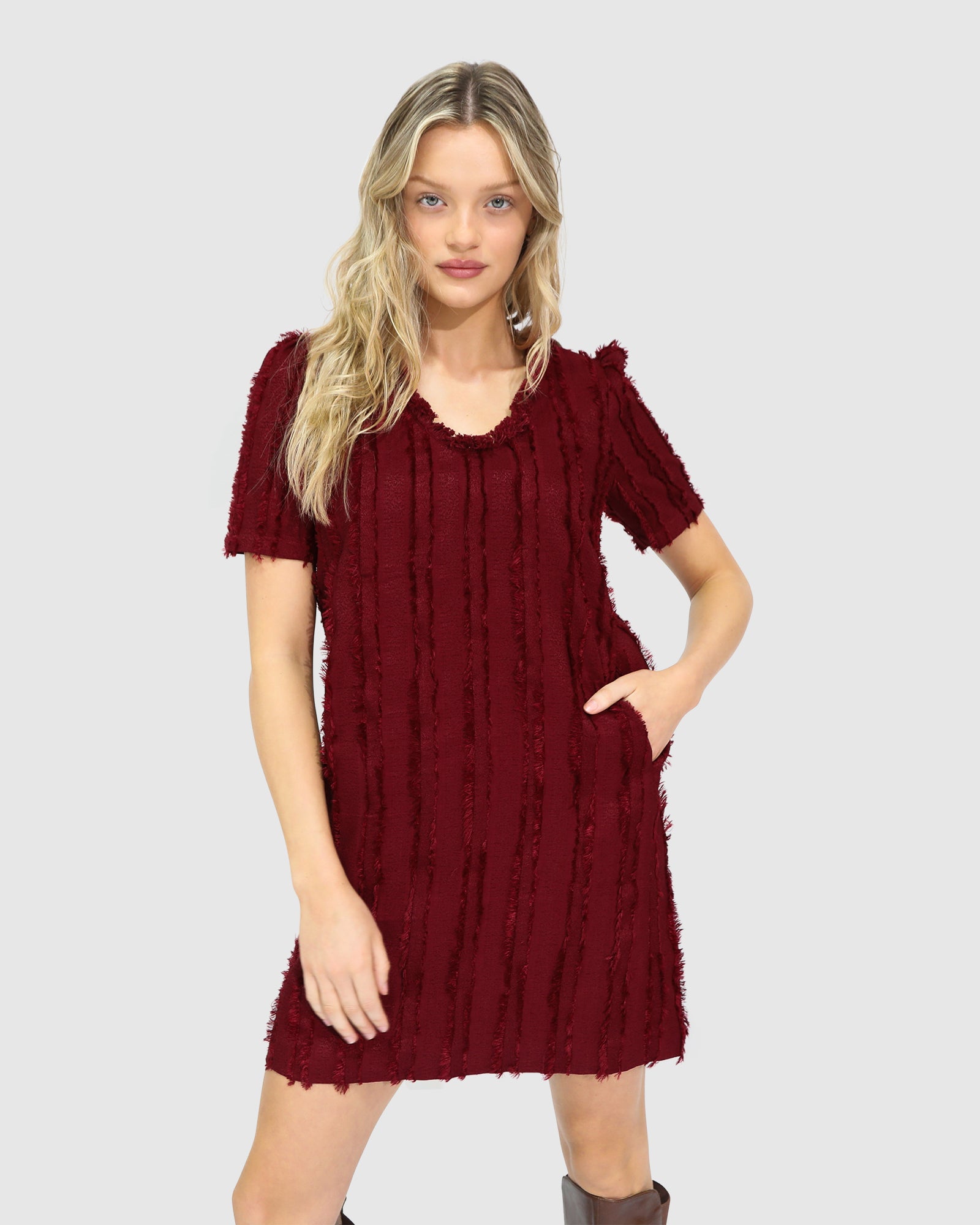 Woman wearing Belle & Bloom's burgundy-coloured Solana Boho Fringe Mini Shift Dress with a frayed V-neckline, textured sleeveless shift silhouette, side-seam pockets, and subtle fringe detail at the hem.