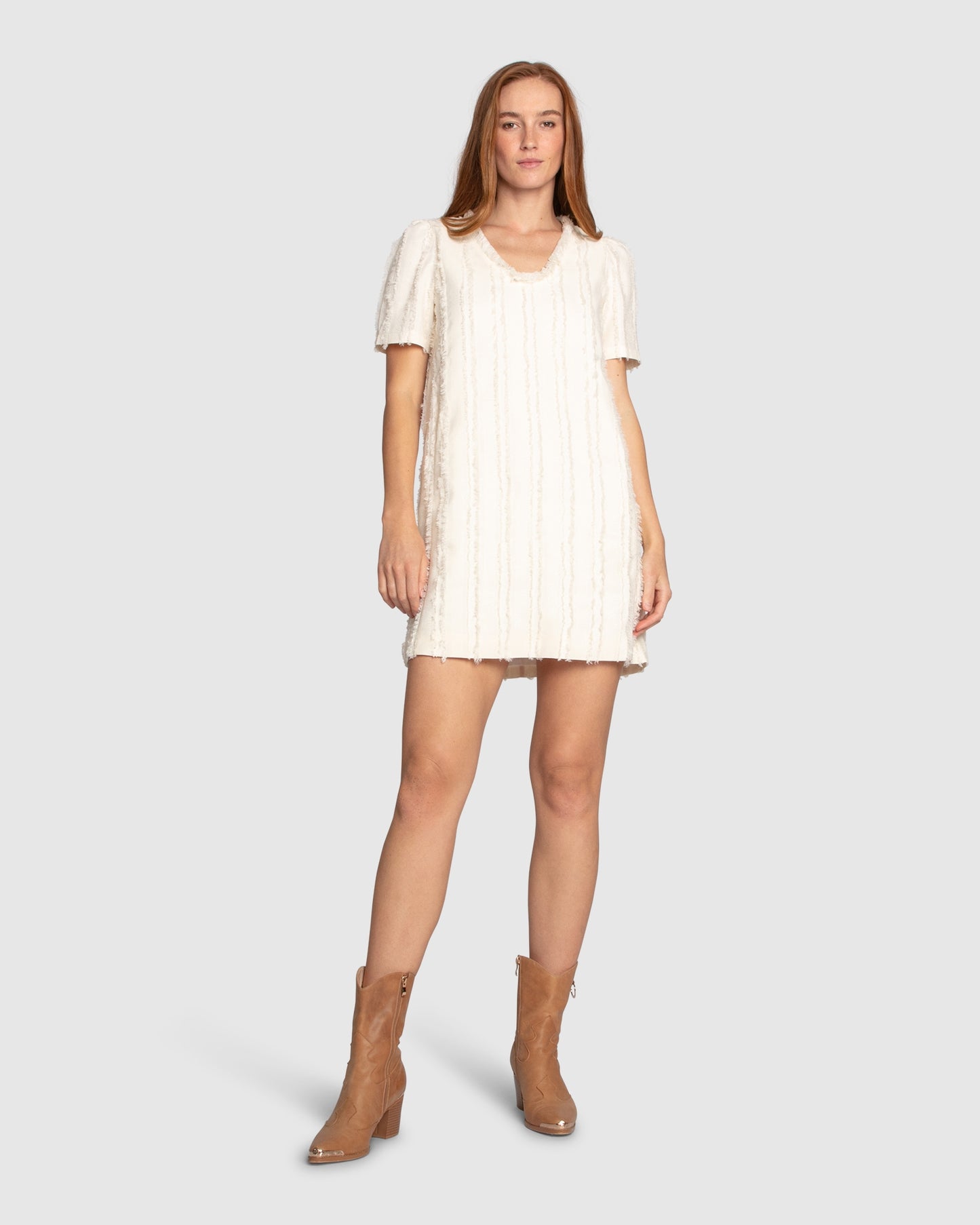 Woman wearing Belle & Bloom's cream-coloured Solana Boho Fringe Mini Shift Dress with a frayed V-neckline, textured sleeveless shift silhouette, side-seam pockets, and subtle fringe detail at the hem.