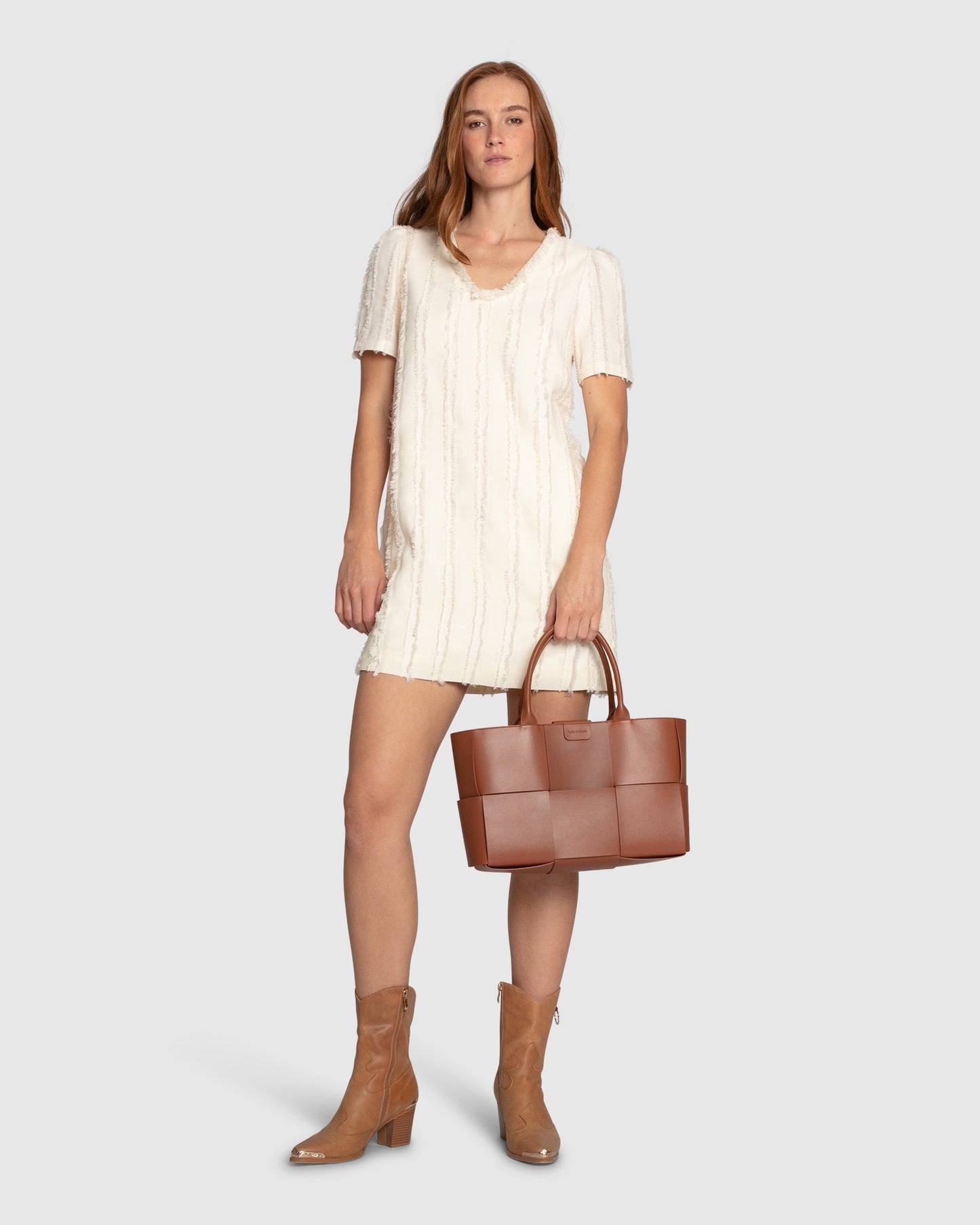 Woman wearing Belle & Bloom's cream-coloured Solana Boho Fringe Mini Shift Dress with a frayed V-neckline, textured sleeveless shift silhouette, side-seam pockets, and subtle fringe detail at the hem.