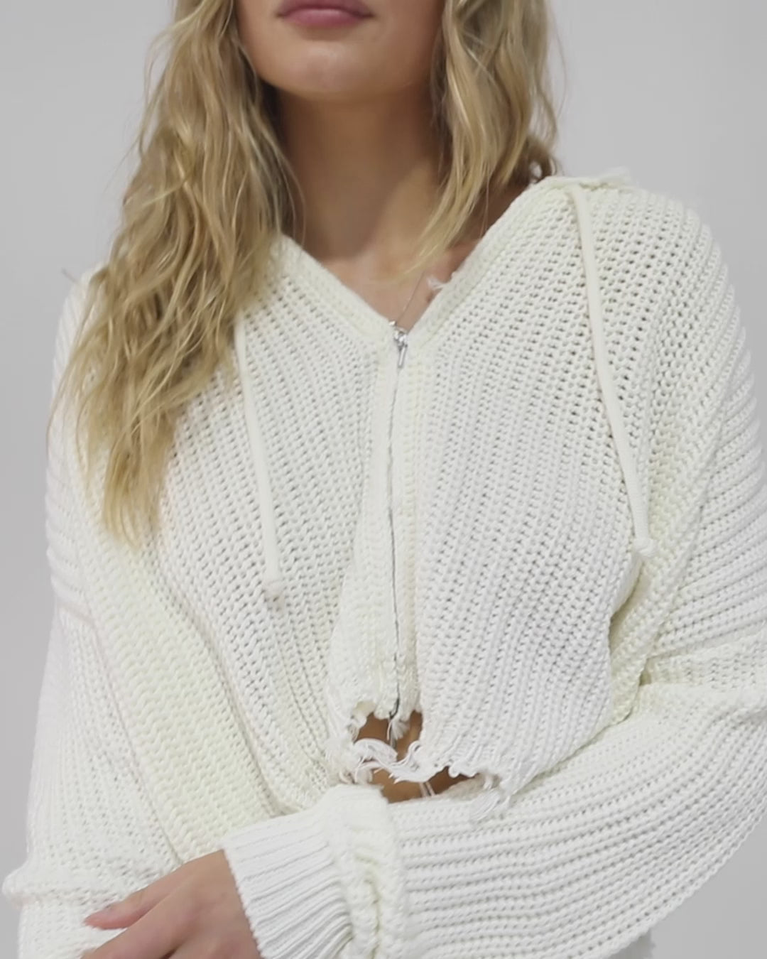 Woman wearing the Another Love Fringe Knit Zip Cardigan in cream, featuring chunky knit texture, zip front, drawstring hood, and fringed cropped hem – Belle and Bloom knitwear.