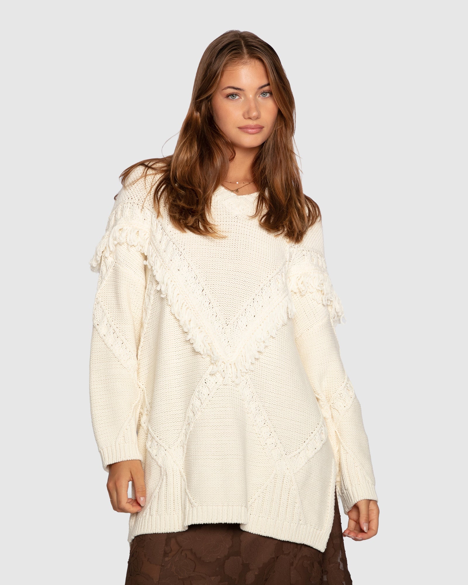 Woman wearing a cream-colored sweater with lace details on a plain background