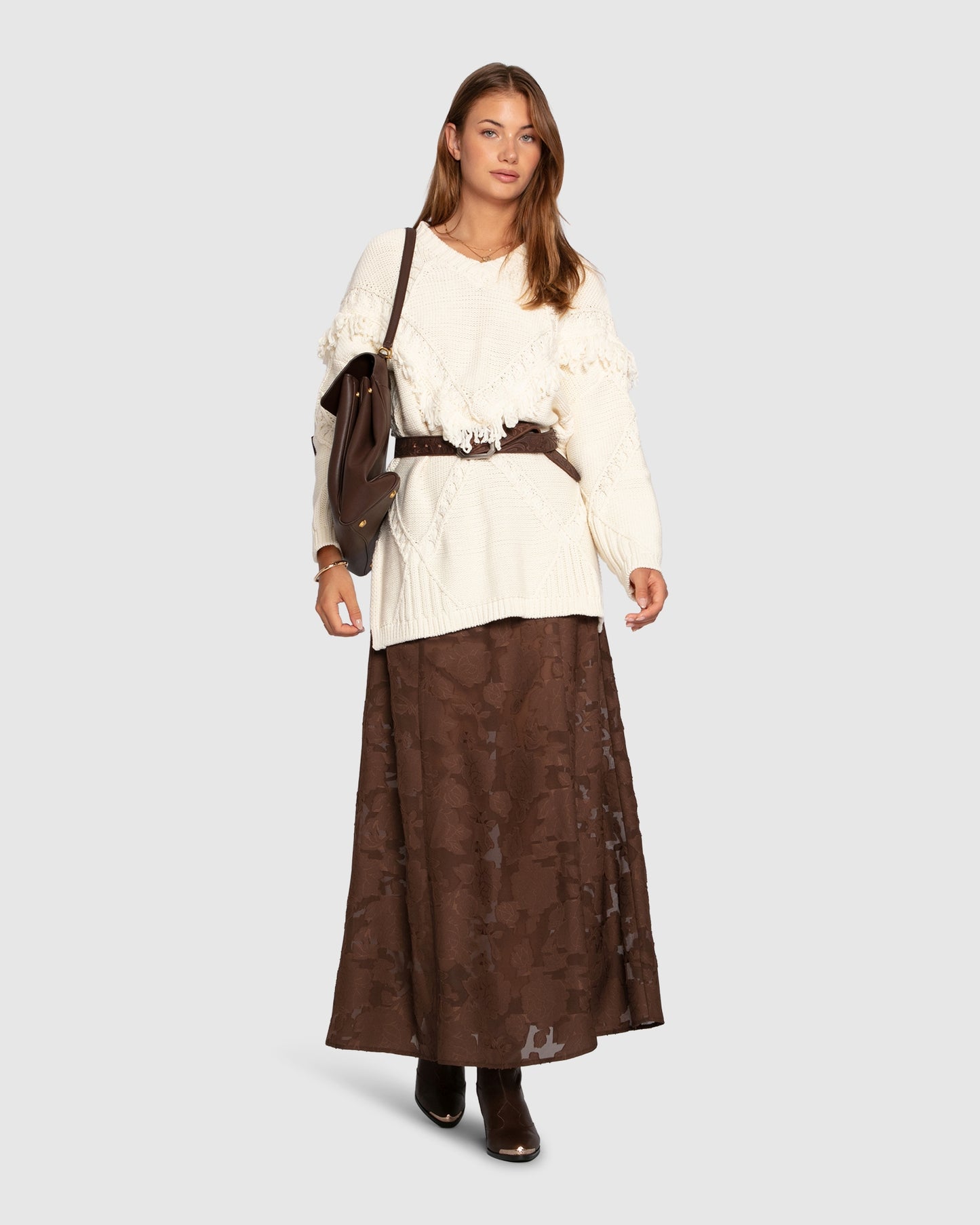 Woman wearing cream oversized knit sweater styled with skirt and belt

