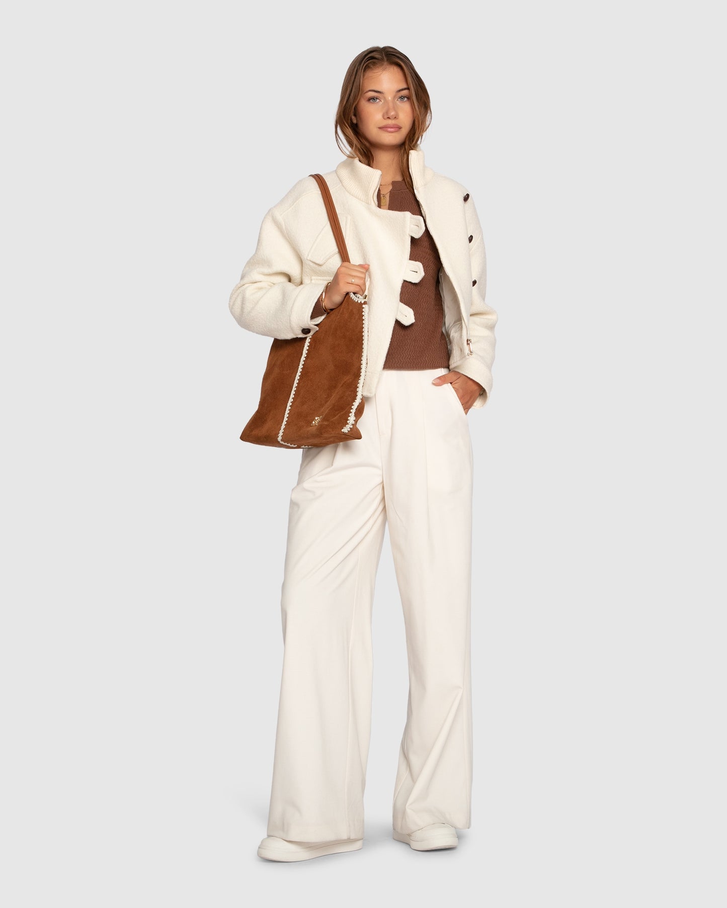 Woman wearing chocolate textured knit top styled with cream coat and trousers