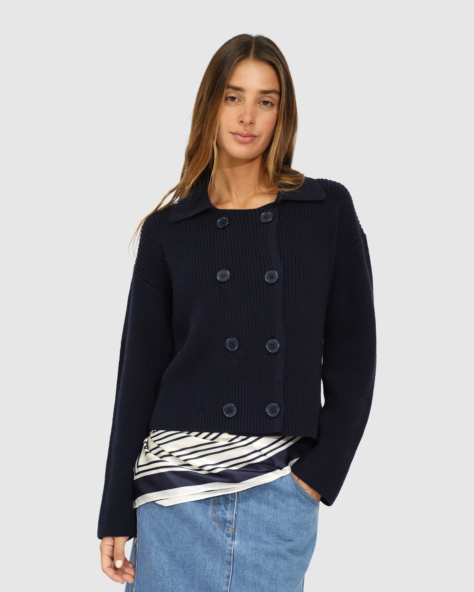 Woman wearing a navy blue jacket over a striped shirt with a light gray background