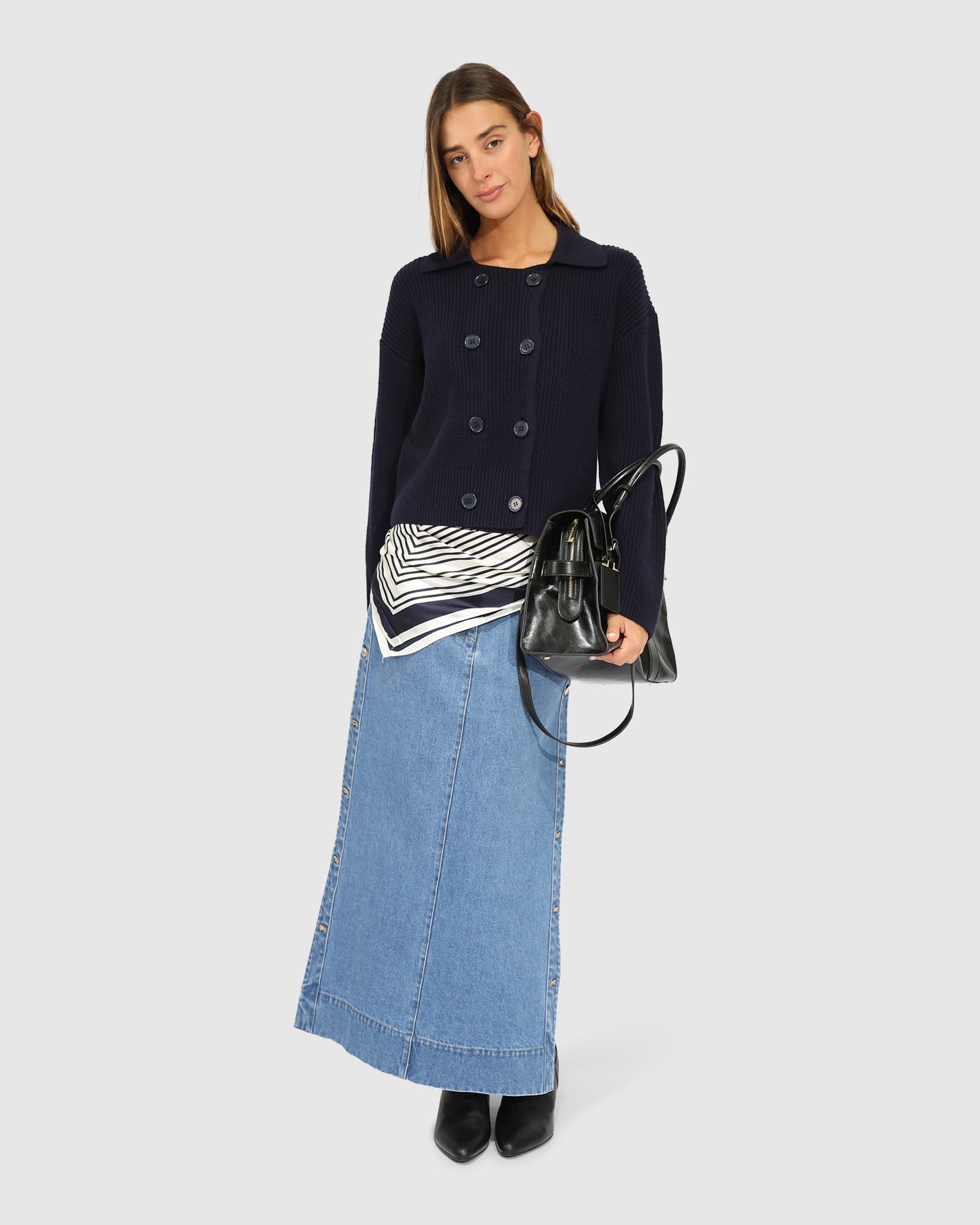 Woman wearing navy rib knit cardi jacket styled with denim skirt, satin scarf, leather bag and boots