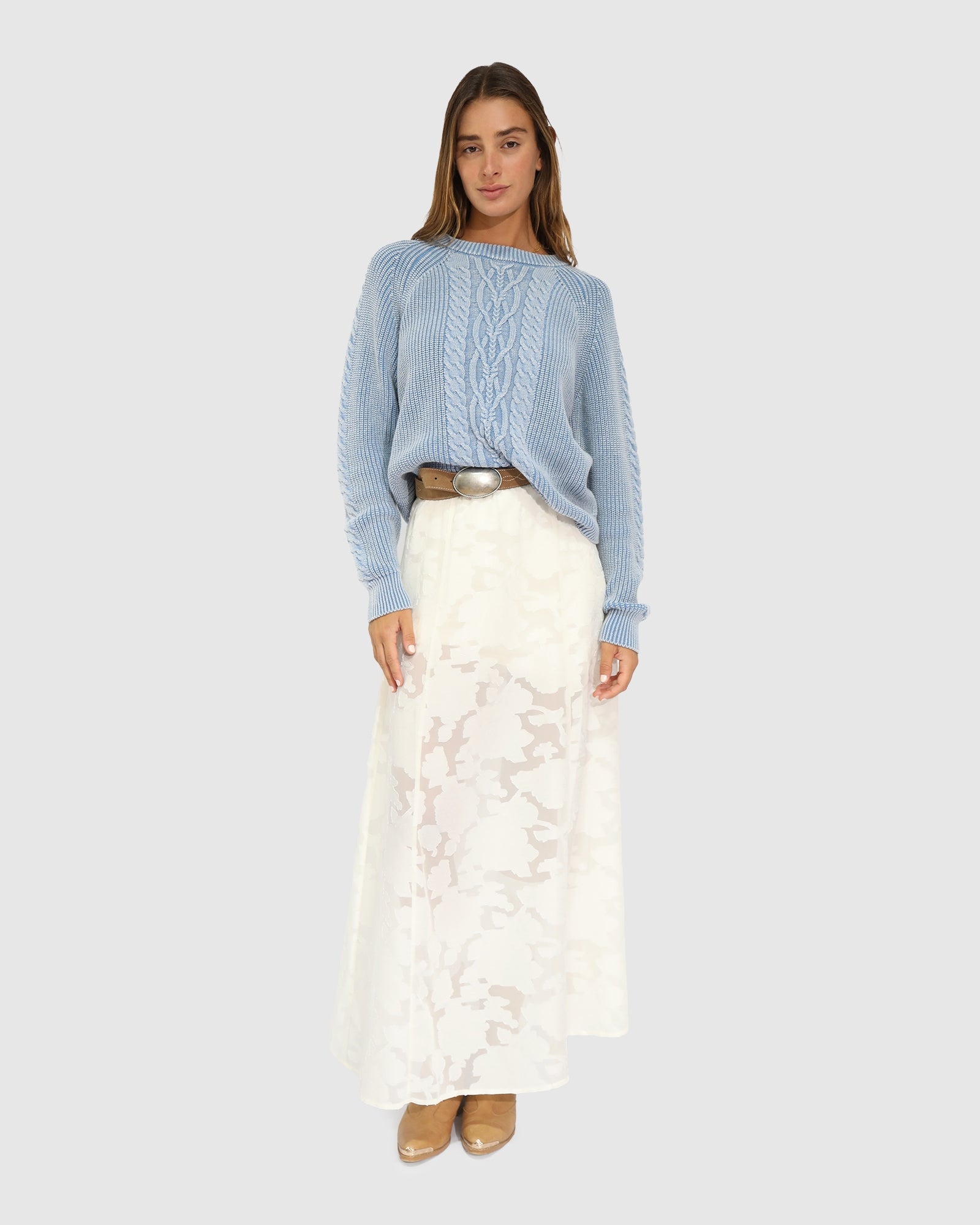 Woman wearing a blue sweater and white lace skirt on a light gray background
