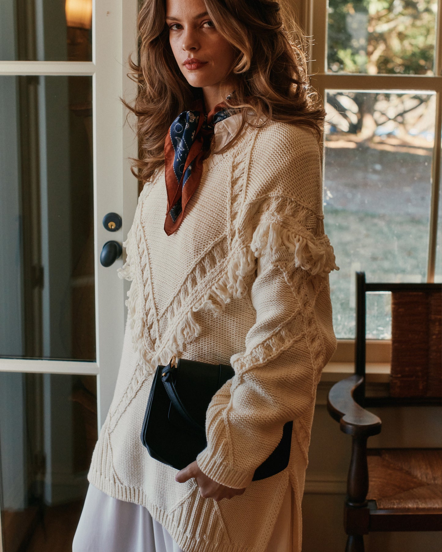 Woman wearing a cream knit sweater wth ruffled details indoors.