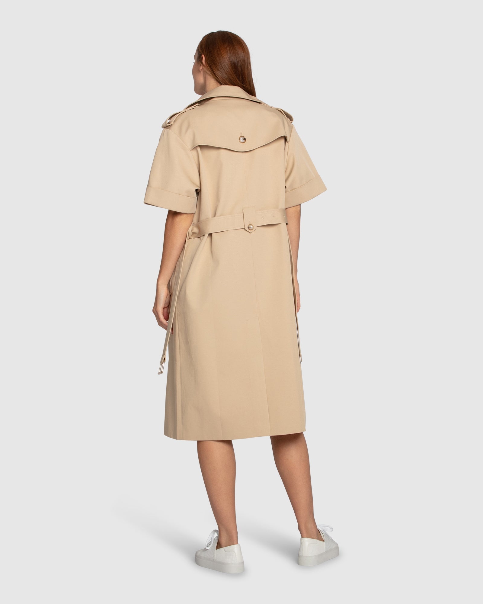 ack view of Belle & Bloom Dust & Daring Short Sleeve Trench Style Dress in beige, featuring belt tie, storm flap detail and knee-length hem.