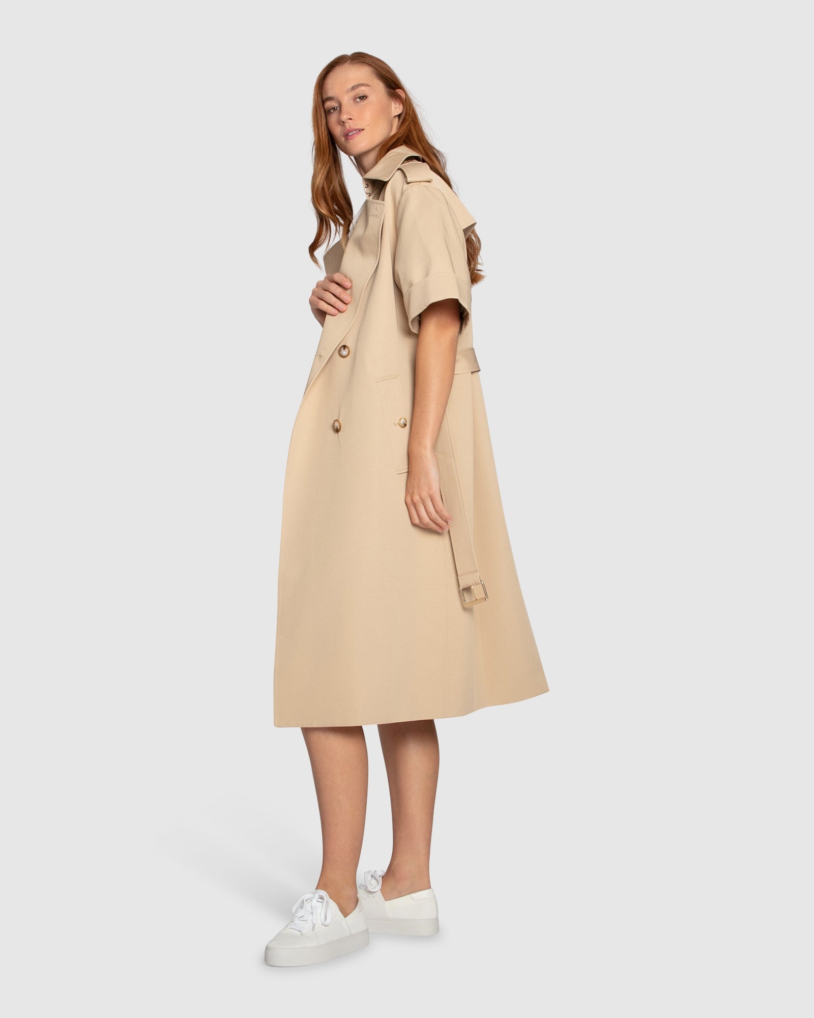 Side angle of Belle & Bloom Dust & Daring Short Sleeve Trench Style Dress in beige, showing short sleeves, belted waist and structured trench silhouette.