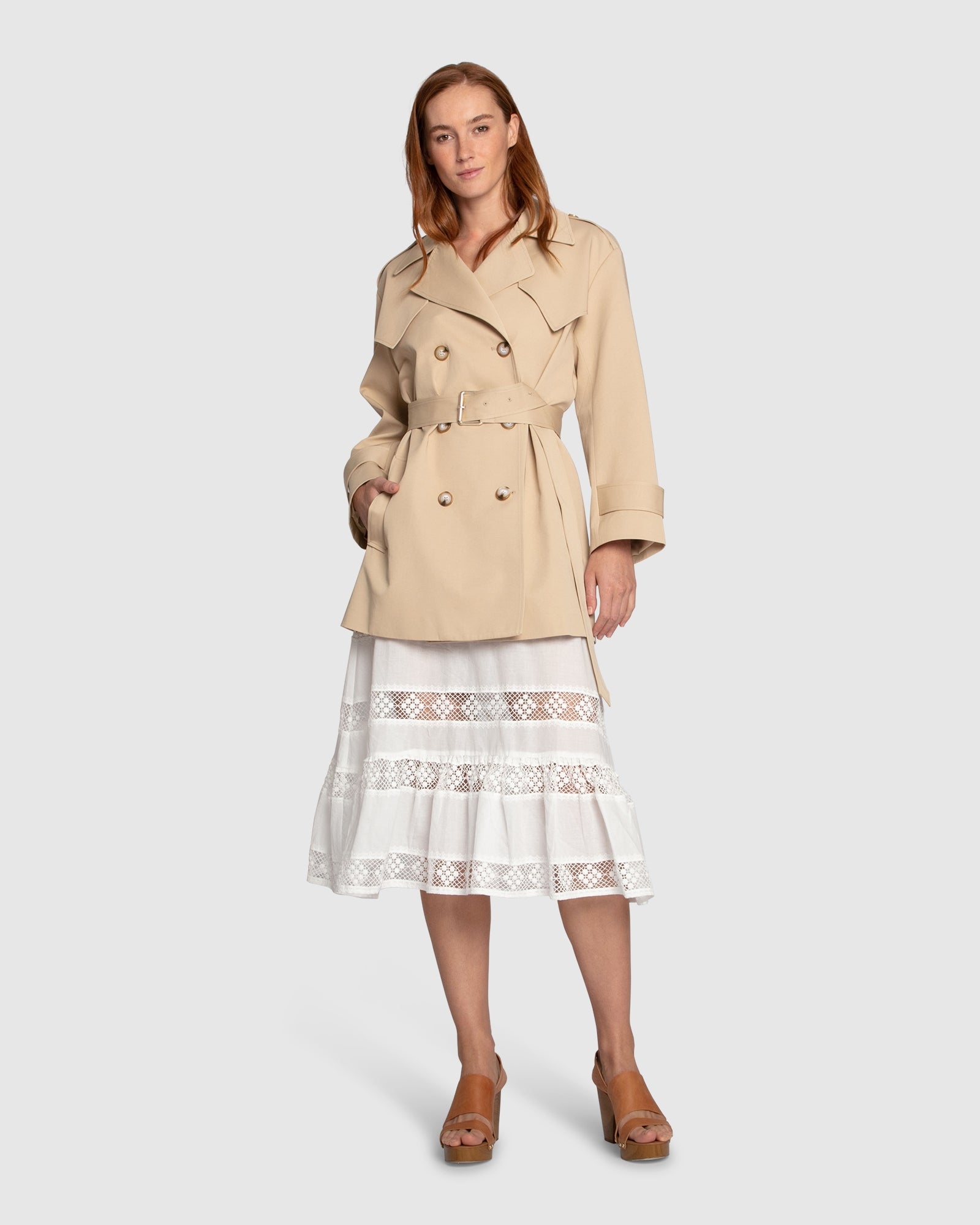 Woman wearing the Whispers of Verona Trench Coat in light camel, featuring a longline double-breasted silhouette, belted waist, storm flap, and classic lapels – Belle and Bloom outerwear.