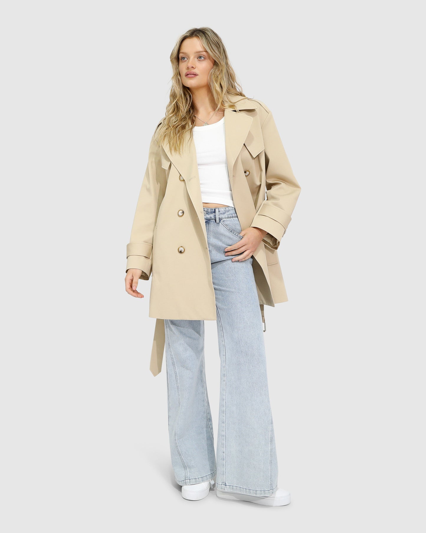 Woman wearing the Whispers of Verona Trench Coat in light camel, featuring a longline double-breasted silhouette, belted waist, storm flap, and classic lapels – Belle and Bloom outerwear.
