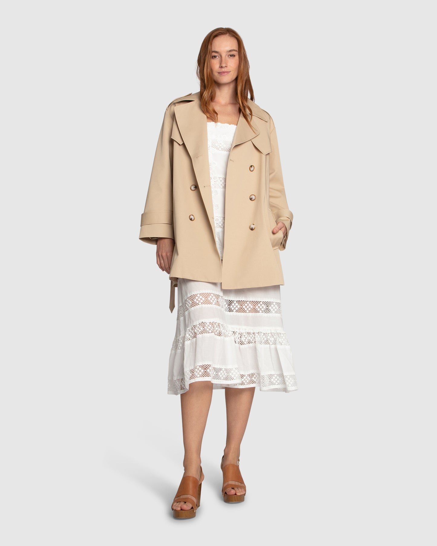 Woman wearing the Whispers of Verona Trench Coat in light camel, featuring a longline double-breasted silhouette, belted waist, storm flap, and classic lapels – Belle and Bloom outerwear.