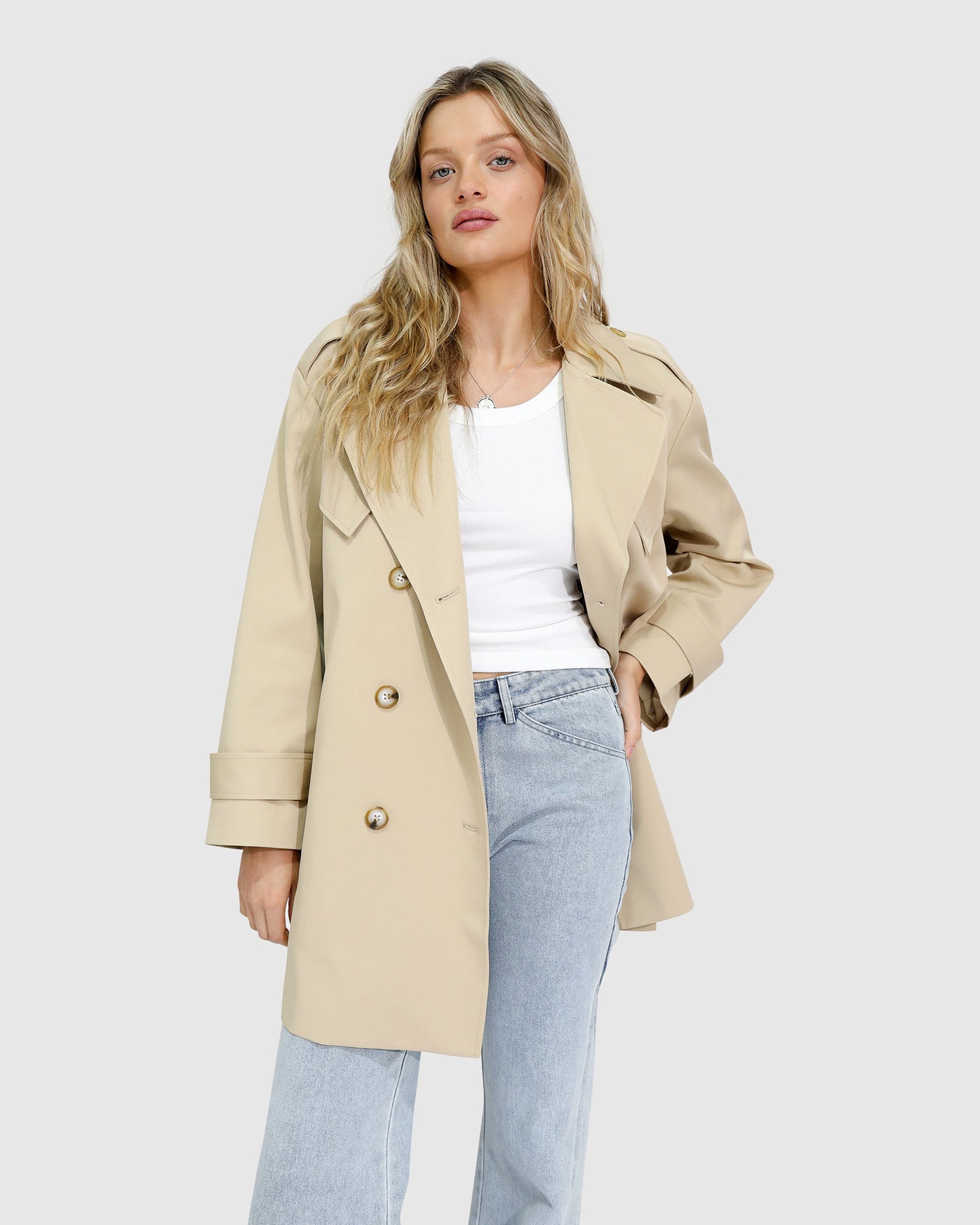 Woman wearing the Whispers of Verona Trench Coat in light camel, featuring a longline double-breasted silhouette, belted waist, storm flap, and classic lapels – Belle and Bloom outerwear.