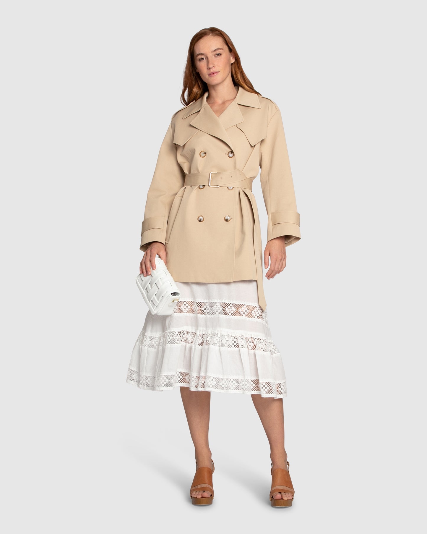Woman wearing the Whispers of Verona Trench Coat in light camel, featuring a longline double-breasted silhouette, belted waist, storm flap, and classic lapels – Belle and Bloom outerwear.