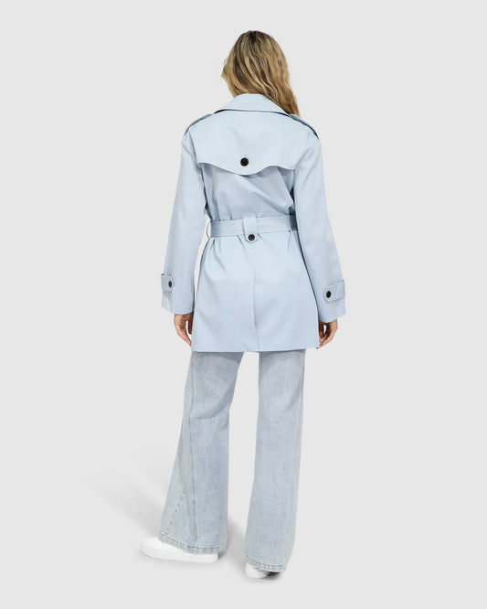 Back view of woman wearing the Whispers of Verona Trench Coat in sky blue, featuring a longline double-breasted silhouette, belted waist, storm flap, and classic lapels – Belle and Bloom outerwear.