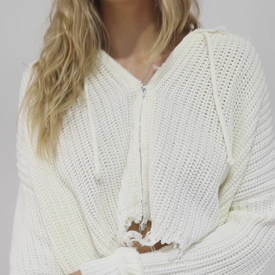 Woman wearing the Another Love Fringe Knit Zip Cardigan in cream, featuring chunky knit texture, zip front, drawstring hood, and fringed cropped hem – Belle and Bloom knitwear.